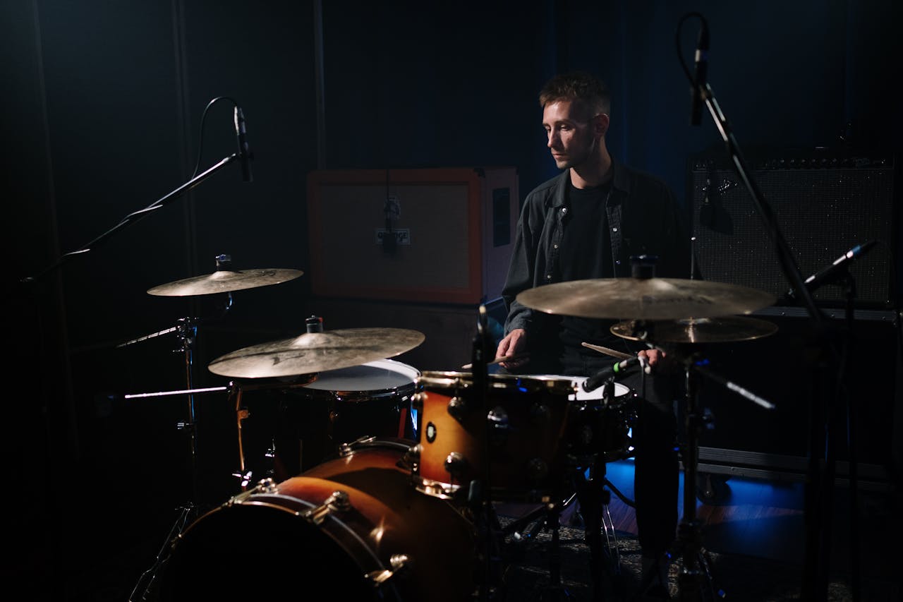 Male musician playing drums in a dimly lit studio with microphones set up for recording.